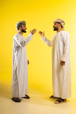 Greeting and peace, the concept of reception and welcome, friendship and building relationships, a portrait of two Arab Gulf Omani men wearing the dishdasha and turban shaking hands, gestures of happiness and joy, yellow background.