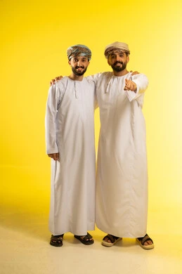Specifying a certain location, pointing to something, a portrait of two Arab Gulf Omani men wearing the dishdasha and turban, pointing with their index fingers, looking at the cameras with gestures of happiness and joy, caring about their appearance, yellow background.