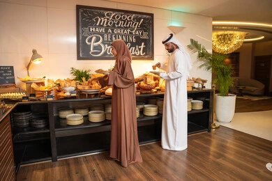 اطباق متنوعه ومختلفه من المأكولات والمخبوزات الشهية والطارجة ،اختيار طبق الفطور ، الاستمتاع بتناول طعام الفطور، قضاء اوقات ممتعه في عطلة نهاية الاسبوع,مفهوم الاسره السعيده, زوجان عربيان اماراتيان  يرتديان الزي التقليدي الاماراتي يغرفان الطعام من البوفيه المفتوح في مطعم فاخر
