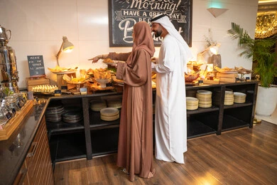 اختيار طبق الفطور ، الاستمتاع بتناول طعام الفطور، قضاء اوقات ممتعه في عطلة نهاية الاسبوع,مفهوم الاسره السعيده, زوجان عربيان اماراتيان  يرتديان الزي التقليدي الاماراتي يغرفان الطعام من البوفيه المفتوح في مطعم فاخر, اطباق متنوعه ومختلفه من المأكولات والمخبوزات الشهية والطارجة