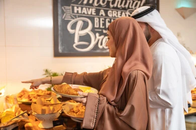 المأكولات والمخبوزات الشهية والطازجة ،اطباق متنوعه ومختلفه ،اختيار طبق الفطور ، الاستمتاع بتناول طعام الفطور، قضاء اوقات ممتعه في عطلة نهاية الاسبوع,مفهوم الاسره السعيده, زوجان عربيان اماراتيان  يرتديان الزي التقليدي الاماراتي يغرفان الطعام من البوفيه المفتوح
