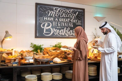اطباق متنوعه ومختلفه من المأكولات والمخبوزات الشهية والطارجة ،اختيار طبق الفطور ، الاستمتاع بتناول طعام الفطور، قضاء اوقات ممتعه في عطلة نهاية الاسبوع,مفهوم الاسره السعيده, زوجان عربيان اماراتيان  يرتديان الزي التقليدي الاماراتي يغرفان الطعام من البوفيه المفتوح في مطعم فاخر