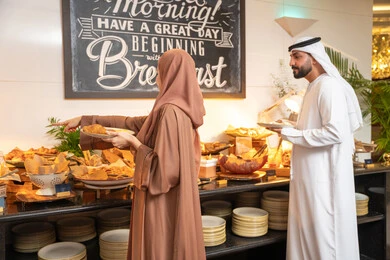 قضاء اوقات ممتعه في عطلة نهاية الاسبوع,مفهوم الاسره السعيده, زوجان عربيان اماراتيان  يرتديان الزي التقليدي الاماراتي يغرفان الطعام من البوفيه المفتوح في مطعم فاخر, الاستمتاع بتناول طعام الفطور, اطباق متنوعه ومختلفه من المأكولات والمخبوزات الشهية والطارجة