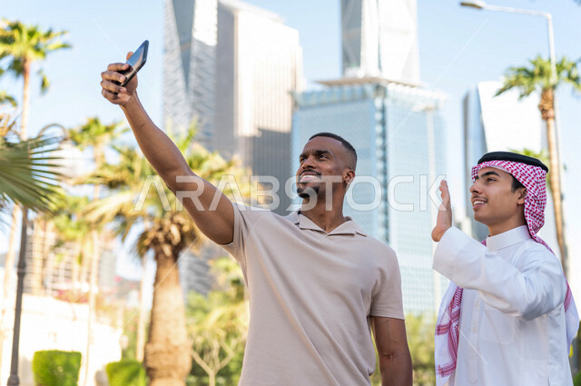 Two smiling Saudi Arabian Gulf Arabs standing next to each other and taking a selfie, a memorial photo, a friendship meeting, spending a good time in King Abdullah Financial City (KAFED) in Riyadh in the Kingdom of Saudi Arabia