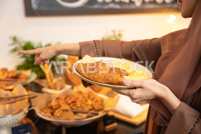 السرور والاستمتاع خارج المنزل، المأكولات والمخبوزات الشهية والطازجة ،اطباق متنوعه ومختلفه ،اختيار طبق الفطور من البوفيه المفتوح، قضاء اوقات ممتعه في عطلة نهاية الاسبوع, صزرو مقربة لسيدة عربية خليجية اماراتية تحمل بيدها طبق الطعام