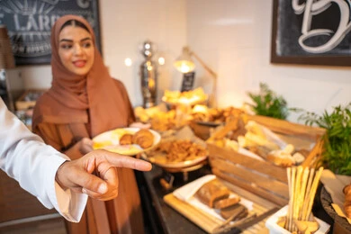 Delicious and fresh foods and pastries, a variety of different dishes, choosing a breakfast dish, enjoying breakfast, spending enjoyable times on the weekend, the concept of a happy family, an Emirati Arab couple wearing traditional Emirati attire serving food from the open buffet.