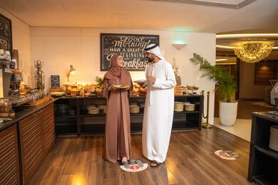 الاستمتاع بتناول طعام الفطور، قضاء اوقات ممتعه في عطلة نهاية الاسبوع,مفهوم الاسره السعيده, زوجان عربيان اماراتيان  يرتديان الزي التقليدي الاماراتي يغرفان الطعام من البوفيه المفتوح في مطعم فاخر, اطباق متنوعه ومختلفه من المأكولات والمخبوزات الشهية والطارجة