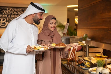 اختيار طبق الفطور ، الاستمتاع بتناول طعام الفطور، قضاء اوقات ممتعه في عطلة نهاية الاسبوع,مفهوم الاسره السعيده, زوجان عربيان اماراتيان  يرتديان الزي التقليدي الاماراتي يغرفان الطعام من البوفيه المفتوح في مطعم فاخر, اطباق متنوعه ومختلفه من المأكولات والمخبوزات الشهية والطارجة