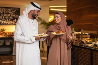 الاستمتاع بتناول طعام الفطور، قضاء اوقات ممتعه في عطلة نهاية الاسبوع,مفهوم الاسره السعيده, زوجان عربيان اماراتيان  يرتديان الزي التقليدي الاماراتي يغرفان الطعام من البوفيه المفتوح في مطعم فاخر, اطباق متنوعه ومختلفه من المأكولات والمخبوزات الشهية والطارجة