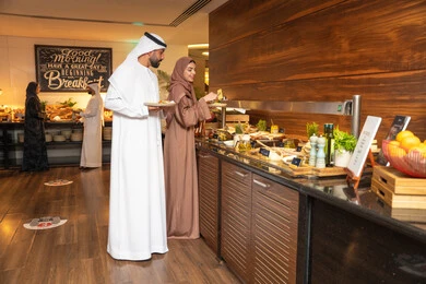 قضاء اوقات ممتعه في عطلة نهاية الاسبوع,مفهوم الاسره السعيده, زوجان عربيان اماراتيان  يرتديان الزي التقليدي الاماراتي يغرفان الطعام من البوفيه المفتوح في مطعم فاخر, الاستمتاع بتناول طعام الفطور, اطباق متنوعه ومختلفه من المأكولات والمخبوزات الشهية والطارجة