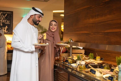 Gestures of happiness, delicious and fresh foods and pastries, diverse and different dishes, choosing a breakfast dish, enjoying having breakfast, spending enjoyable times on the weekend, the concept of a happy family, an Emirati Arab couple wearing traditional Emirati attire serving food from the open buffet. Gestures of happiness, delicious and fresh foods and pastries, diverse and different dishes, choosing a breakfast dish, enjoying having breakfast, spending enjoyable times on the weekend, the concept of a happy family, an Emirati Arab couple wearing traditional Emirati attire serving food from the open buffet.