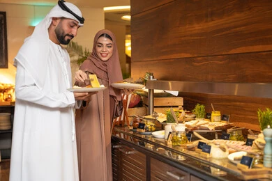Delicious and fresh foods and pastries, a variety of different dishes, choosing a breakfast dish, enjoying breakfast, spending enjoyable times on the weekend, the concept of a happy family, an Emirati Arab couple wearing traditional Emirati attire serving food from the open buffet. Delicious and fresh foods and pastries, a variety of different dishes, choosing a breakfast dish, enjoying breakfast, spending enjoyable times on the weekend, the concept of a happy family, an Emirati Arab couple wearing traditional Emirati attire serving food from the open buffet.