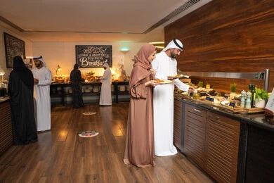 مفهوم الاسره السعيده, زوجان عربيان اماراتيان  يرتديان الزي التقليدي الاماراتي يغرفان الطعام من البوفيه المفتوح في مطعم فاخر, الاستمتاع بتناول طعام الفطور, قضاء اوقات ممتعه في عطلة نهاية الاسبوع, اطباق متنوعه ومختلفه من المأكولات والمخبوزات الشهية والطارجة