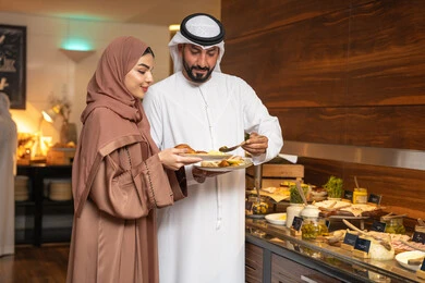 المأكولات والمخبوزات الشهية والطازجة ،اطباق متنوعه ومختلفه ،اختيار طبق الفطور ، الاستمتاع بتناول طعام الفطور، قضاء اوقات ممتعه في عطلة نهاية الاسبوع,مفهوم الاسره السعيده, زوجان عربيان اماراتيان  يرتديان الزي التقليدي الاماراتي يغرفان الطعام من البوفيه المفتوح