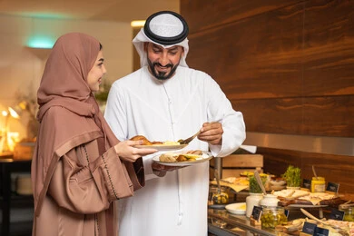 اطباق متنوعه ومختلفه من المأكولات والمخبوزات الشهية والطارجة ،اختيار طبق الفطور ، الاستمتاع بتناول طعام الفطور، قضاء اوقات ممتعه في عطلة نهاية الاسبوع,مفهوم الاسره السعيده, زوجان عربيان اماراتيان  يرتديان الزي التقليدي الاماراتي يغرفان الطعام من البوفيه المفتوح في مطعم فاخر