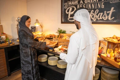 اطباق متنوعه ومختلفه من المأكولات والمخبوزات الشهية والطارجة ،اختيار طبق الفطور ، الاستمتاع بتناول طعام الفطور، قضاء اوقات ممتعه في عطلة نهاية الاسبوع, زوجان عربيان اماراتيان  يرتديان الزي التقليدي الاماراتي يغرفان الطعام من البوفيه المفتوح في مطعم فاخر