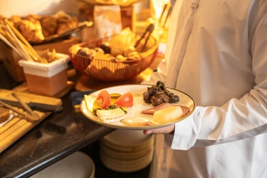 Enjoying outside the home, spending enjoyable times on the weekend, a variety of different dishes of delicious and fresh foods and pastries, choosing a breakfast dish, an Emirati Gulf Arab man wearing traditional attire serving food from the open buffet in a luxury restaurant.