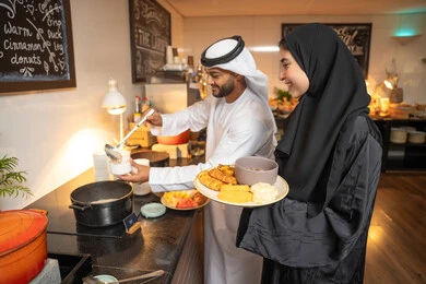 اطباق متنوعه ومختلفه من المأكولات والمخبوزات الشهية والطارجة ،اختيار طبق الفطور ، الاستمتاع بتناول طعام الفطور، قضاء اوقات ممتعه في عطلة نهاية الاسبوع, زوجان عربيان اماراتيان  يرتديان الزي التقليدي الاماراتي يغرفان الطعام من البوفيه المفتوح في مطعم فاخر