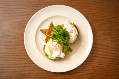 A useful, healthy, and quick dish, following dietary regimens, delicious foods and meals rich in healthy proteins, a breakfast meal, a picture of a plate containing two pieces of toast topped with avocado butter and feta cheese garnished with fresh arugula herbs.