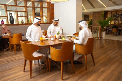 A fun and social gathering, enjoying delicious food, exchanging conversations and news, sharing enjoyable moments with friends, building successful social relationships, Emirati Gulf Arab friends wearing kandura and ghutrah sitting in one of the luxurious cafes in the kingdom.