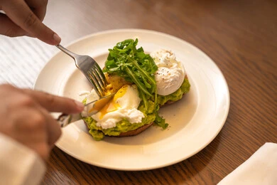 A useful, healthy, and quick dish, following dietary regimens, delicious foods and meals rich in healthy proteins, a breakfast meal, a picture of a plate containing two pieces of toast topped with avocado butter and feta cheese garnished with fresh arugula herbs.