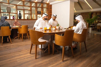 مفهوم مشاركة الأصدقاء الأوقات الممتعة, جلسة وناسة وتعارف، الاستمتاع بتناول الاطعمة اللذيذة, تبادل الأحاديث والاخبار, بناء علاقات اجتماعية ناجحة, أصدقاء عرب خليجيون اماراتيون يرتدون الكندورة والغترة يجلسون في إحدى الكافيهات الفاخرة في المملكة