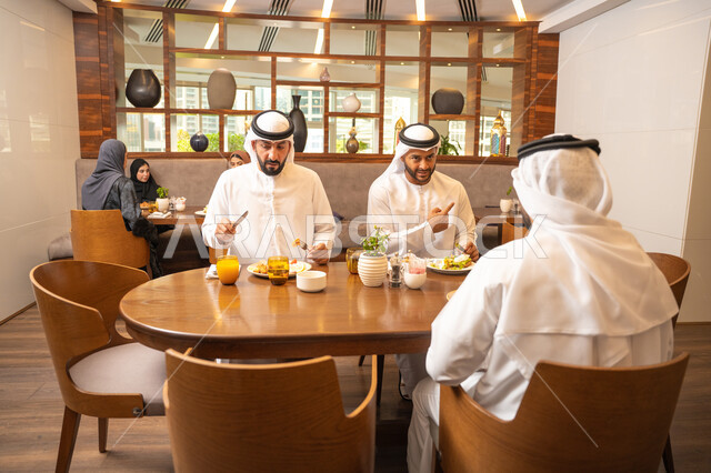 بناء علاقات اجتماعية ناجحة, مفهوم مشاركة الأصدقاء الأوقات الممتعة, جلسة وناسة وتعارف، الاستمتاع بتناول الاطعمة اللذيذة, تبادل الأحاديث والاخبار, أصدقاء عرب خليجيون اماراتيون يرتدون الكندورة والغترة يجلسون في إحدى الكافيهات الفاخرة في المملكة