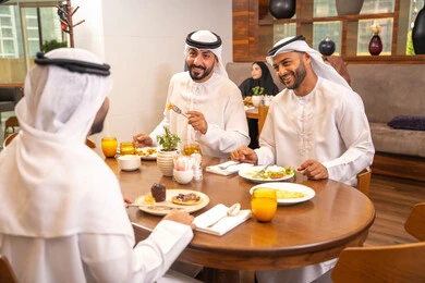 The concept of sharing enjoyable times with friends, a fun and social gathering, enjoying delicious food, exchanging conversations and news, building successful social relationships, Emirati Gulf Arab friends wearing kandura and ghutrah sitting in one of the luxurious cafes in the kingdom.