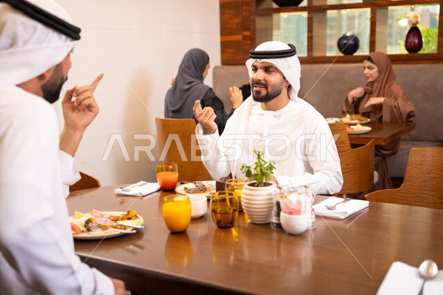 Enjoying desserts and natural juice, exchanging conversations and news, sharing enjoyable moments with friends, building successful social relationships, two Emirati Gulf Arab friends wearing kandura and ghutrah sitting in one of the luxurious cafes in the kingdom.
