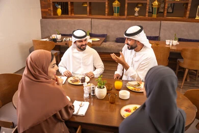 تناول وجبات طعام لذيذة، جلسة وناسة وتعارف، نقاشات و حوارات عائليه على مائدة الطعام, عائلة عربية اماراتية خليجيه يرتدون الزي التقليدي يجلسون في مطعم فاخر،  قضاء أوقات عائليه ممتعه في عطلة نهاية الاسبوع, صداقات وبناء علاقات اجتماعيه