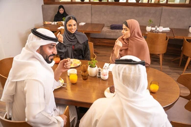 Enjoying delicious meals, a fun and social gathering, family discussions and conversations at the dining table, an Emirati Arab Gulf family dressed in traditional attire sitting in a luxurious restaurant, spending enjoyable family time on the weekend, friendships and building social relationships.