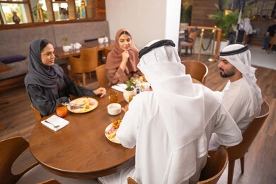 قضاء أوقات عائليه ممتعه في عطلة نهاية الاسبوع, جلسة وناسة وتعارف، نقاشات و حوارات عائليه على مائدة الطعام, عائلة عربية اماراتية خليجيه يرتدون الزي التقليدي يجلسون في مطعم فاخر،  تناول وجبات طعام لذيذة، صداقات وبناء علاقات اجتماعيه