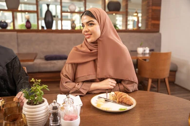الاستمتاع خارج المنزل، سيدة عربية خليجية اماراتية ترتدي العباءة والحجاب تجلس في مطعم فاخر، قضاء اوقات ممتعة في احدى مقاهي الامارات ، تبادل الاحاديث والحوارات،  تناول طعام الفطور، أنشطة شبابية ترفيهية
