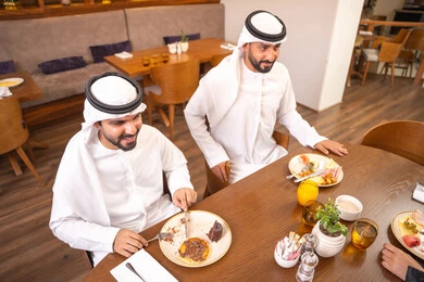Enjoying desserts and natural juice, exchanging conversations and news, sharing enjoyable moments with friends, building successful social relationships, two Emirati Gulf Arab friends wearing kandura and ghutrah sitting in one of the luxurious cafes in the kingdom. Enjoying desserts and natural juice, exchanging conversations and news, sharing enjoyable moments with friends, building successful social relationships, two Emirati Gulf Arab friends wearing kandura and ghutrah sitting in one of the luxurious cafes in the kingdom.