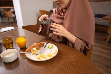 Using a modern and advanced technical device, having a good time at the restaurant, a close-up image of a veiled Emirati Gulf Arab woman wearing an abaya, a young Saudi woman taking a commemorative photo of the food dishes with her mobile phone, enjoying delicious food in restaurants and cafes in the UAE.