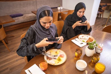 اجتماع في عطلة نهاية الأسبوع، قضاء وقت ممتع بين الإصدقاء، التقاط الصور التذكارية لأطباق الأطعمة والوجبات اللذيذة باستخدام الهاتف المحمول، جلسة وناسة وتعارف، بناء علاقات إجتماعية، مطعم راقي في الامارات، صديقات عربيات خليجيات اماراتيات يجلسن في إحدى المطاعم الفاخرة