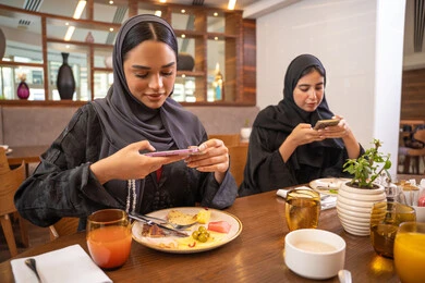 بناء علاقات إجتماعية، اجتماع في عطلة نهاية الأسبوع، قضاء وقت ممتع بين الإصدقاء، التقاط الصور التذكارية لأطباق الأطعمة والوجبات اللذيذة باستخدام الهاتف المحمول، جلسة وناسة وتعارف، مطعم راقي في الامارات، صديقات عربيات خليجيات اماراتيات يجلسن في إحدى المطاعم الفاخرة