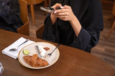 Spending a good time at the restaurant, using a modern and advanced technical device, a close-up image of a veiled Emirati Gulf Arab woman wearing an abaya, a young Saudi woman taking a souvenir photo of the food dishes with her mobile phone, enjoying hot drinks and desserts in restaurants and cafes in the UAE.