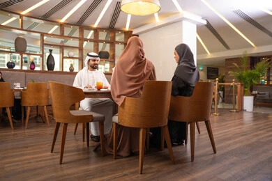 Family discussions and conversations at the dining table, an Emirati Arab Gulf family sitting in a luxurious restaurant, enjoying healthy and delicious meals, spending enjoyable family time on the weekend, making acquaintances and friendships, and building social relationships.