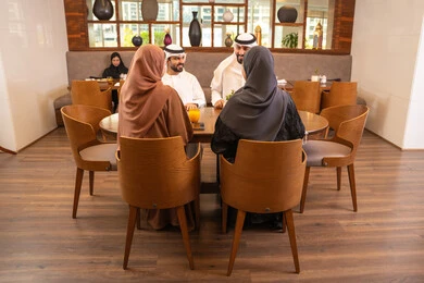 قضاء أوقات عائليه ممتعه في عطلة نهاية الاسبوع, جلسة وناسة وتعارف، نقاشات و حوارات عائليه على مائدة الطعام, عائلة عربية اماراتية خليجيه يرتدون الزي التقليدي يجلسون في مطعم فاخر،  تناول وجبات طعام لذيذة، صداقات وبناء علاقات اجتماعيه