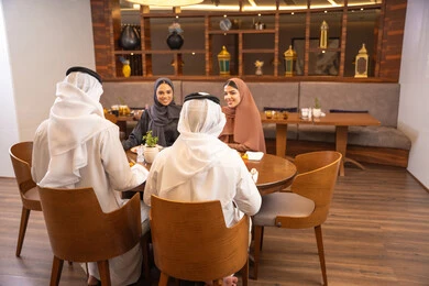 Family discussions and conversations at the dining table, an Emirati Arab Gulf family sitting in a luxurious restaurant, enjoying healthy and delicious meals, spending enjoyable family time on the weekend, making acquaintances and friendships, and building social relationships.