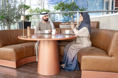 شرب القهوة العربية، قضاء أوقات عائلية ممتعة, التفاهم والترابط الفكري بين الزوجين، رجل عربي خليجي اماراتي يرتدي الكندورة والغترة يجلس فى احد المقاهي يقوم بتبادل الأحاديث مع زوجته في الهواء الطلق
