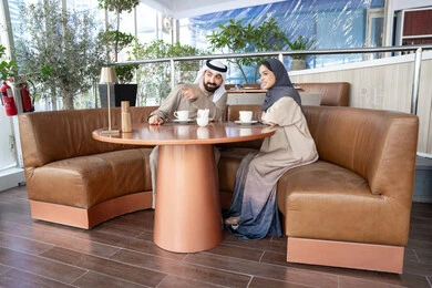 الإشارة باتجاه شيء ما، مشاعر المودة والترابط بين الزوجين، قضاء أوقات ممتعة، رجل عربي خليجي اماراتي يرتدي الكندورة و الغتره يجلس فى احد المقاهي برفقة زوجته ، ايماءات السعادة و السرور