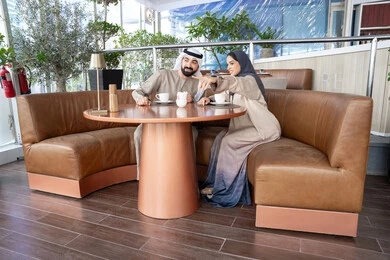 الإشارة باليد نحو شيء معين، مشاعر المودة والترابط بين الزوجين، قضاء أوقات ممتعة، رجل عربي خليجي اماراتي يرتدي الكندورة و الغتره يجلس فى احد المقاهي برفقة زوجته ، ايماءات السعادة و السرور