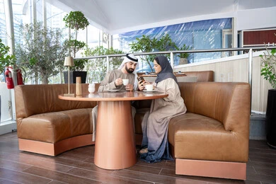 الترفيه والتسلية في العطلة، مفهوم المودة والالفة، الاستمتاع بتناول المشروبات المفضله ، قضاء وقت ممتع في الخارج، رجل عربي خليجي اماراتي يرتدي الكندورة و الغتره يجلس فى احد المقاهي برفقه زوجته يشاهدان الهاتف المحمول، ايماءات السعادة و السرور