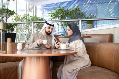 مفهوم المودة والالفة، الترفيه والتسلية في العطلة، الاستمتاع بتناول المشروبات المفضله ، قضاء وقت ممتع في الخارج، رجل عربي خليجي اماراتي يرتدي الكندورة و الغتره يجلس فى احد المقاهي برفقه زوجته ، ايماءات السعادة و السرور مفهوم المودة والالفة، الترفيه والتسلية في العطلة، الاستمتاع بتناول المشروبات المفضله ، قضاء وقت ممتع في الخارج، رجل عربي خليجي اماراتي يرتدي الكندورة و الغتره يجلس فى احد المقاهي برفقه زوجته ، ايماءات السعادة و السرور