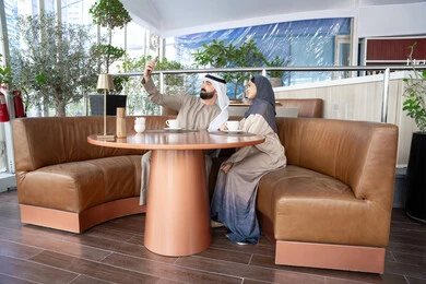 The use of social media, taking commemorative photos via mobile, happy family atmospheres, documenting happy moments, strengthening marital relationships and bonds of love and affection, an Emirati Arab couple wearing traditional attire sitting in one of the cafes in the United Arab Emirates. The use of social media, taking commemorative photos via mobile, happy family atmospheres, documenting happy moments, strengthening marital relationships and bonds of love and affection, an Emirati Arab couple wearing traditional attire sitting in one of the cafes in the United Arab Emirates.