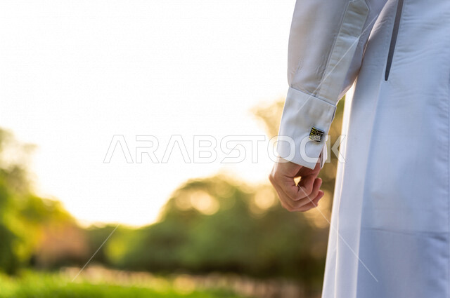 A close-up image of the hand of a Saudi Arabian Gulf man against a background of picturesque nature in one of the gardens of the Kingdom of Saudi Arabia, wearing a Saudi traditional dress