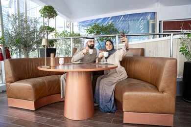 التقاط صور السيلفي التذكارية باستخدام الهاتف المحمول، زوجان عربيان خليجيان اماراتيان يرتديان الزي التقليدي يجلسان فى احد المقاهي بالامارات العربية، تقوية العلاقات الزوجية وروابط الحب والمودة، تناول المشروبات المفضلة