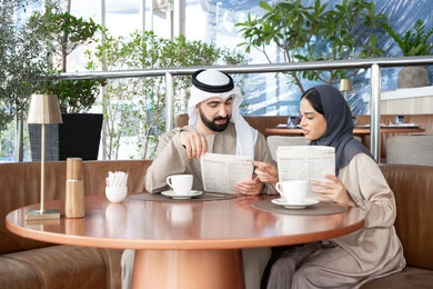 Choosing favorite dishes and drinks from the menu, having a good time at the café, an Emirati Gulf Arab couple dressed in traditional attire sitting in one of the cafés exchanging conversation, a happy family atmosphere.